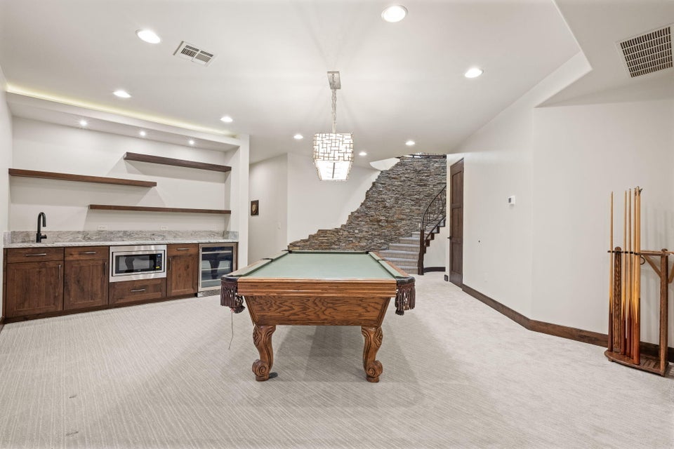 Spacious entertainment area featuring a stone-clad staircase, built-in wet bar with wood cabinetry, integrated microwave, and beverage cooler