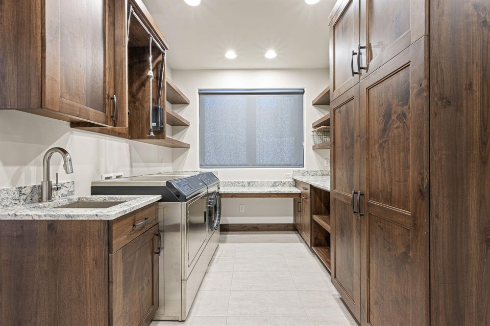 Dedicated utility room featuring extensive wood-finish cabinetry, light-toned countertop surfaces, a built-in sink with a gooseneck faucet, integrated shelving, and recessed lighting