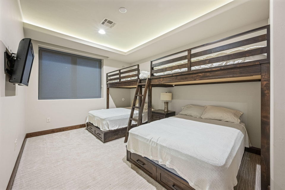 Recessed lighting and cove lighting illuminate a room featuring light-colored carpeting, dark wood-finish baseboards, and a window with a roller shade