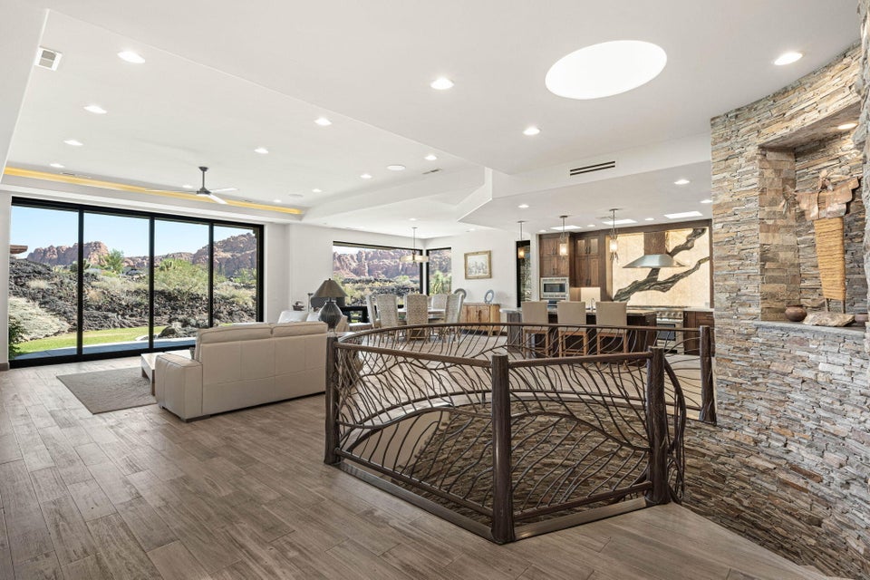 Open concept living space featuring a custom metal railing, stone accent wall, large format wood-finish flooring, recessed lighting, and expansive glass sliding doors