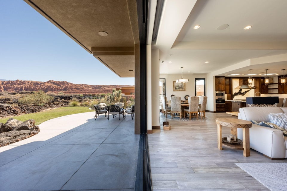 Expansive sliding glass doors opening to a concrete patio, a manicured lawn, and distant natural rock formations