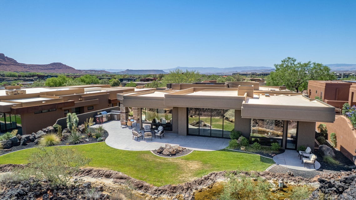 Desert contemporary residence featuring a terraced backyard with a shaped lawn, expansive patio, and integrated outdoor kitchen