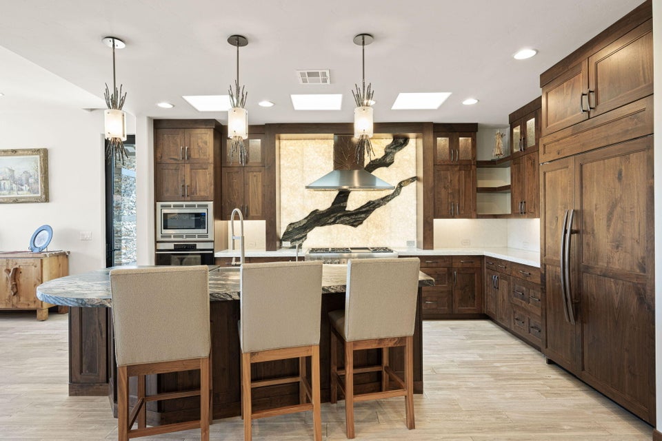 Kitchen featuring dark wood cabinetry, a large center island with seating, integrated panel-front refrigerator, stainless steel appliances, and multiple skylights