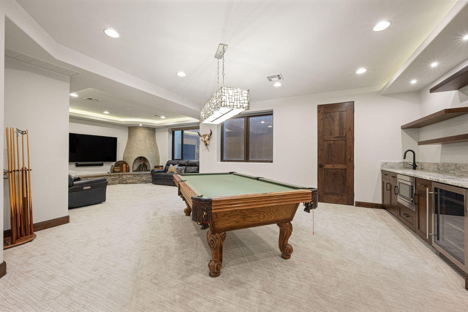 Spacious recreational room featuring a stone fireplace, recessed lighting, and a wet bar with granite countertops
