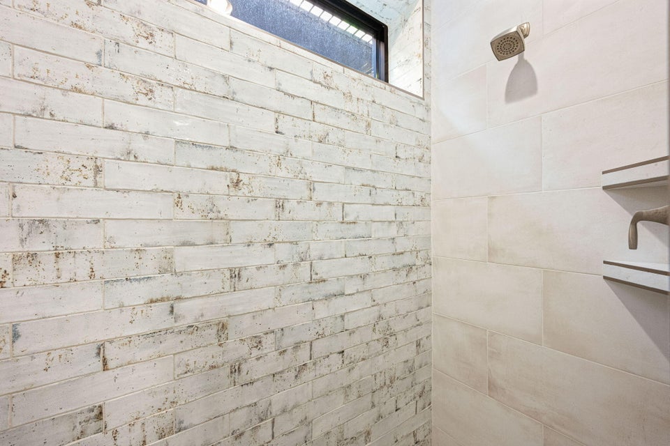 Shower featuring a distressed white brick-style wall, large format tile, a bronze-finish showerhead, and a built-in shelving niche with bronze-finish fixtures