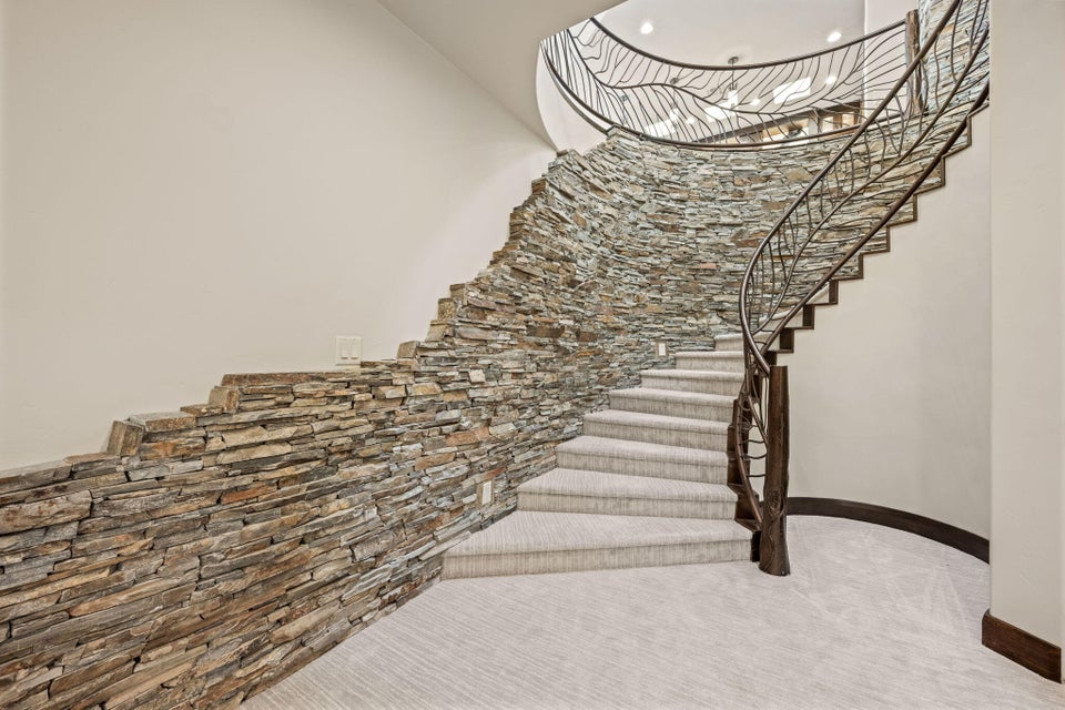 Curved staircase featuring a stone accent wall, wrought iron railing, wood newel post, and light-colored carpeted treads