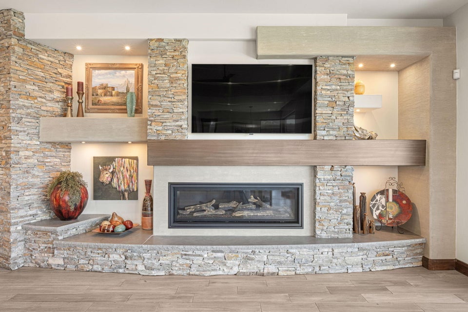 Custom stone-stacked fireplace wall with an integrated media niche, recessed lighting, wood-finish mantel, and built-in stone hearth