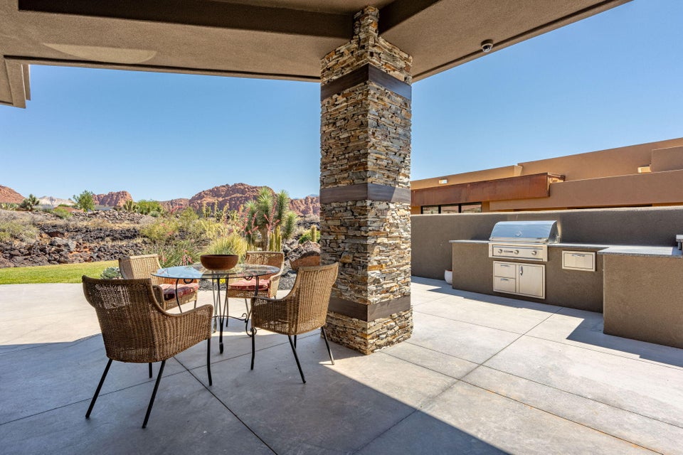 Covered patio featuring a stacked stone pillar, integrated outdoor kitchen with stainless steel grill, concrete flooring, and desert landscape backdrop