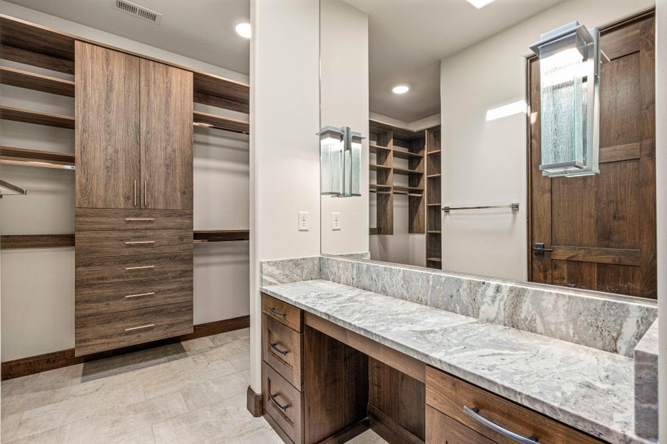 Dressing area featuring a vanity with a large mirror, stone countertop, built-in storage, and integrated shelving