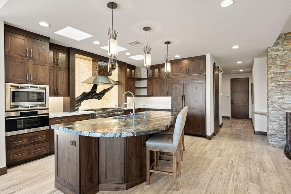 Gourmet kitchen featuring a large stone countertop island, integrated stainless steel appliances, custom wood cabinetry, skylights, and wood-finish flooring