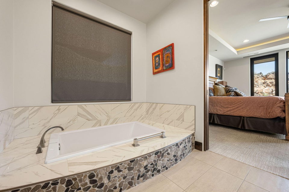 Soaking tub with a marbled tile surround and river rock accent, featuring a privacy roller shade