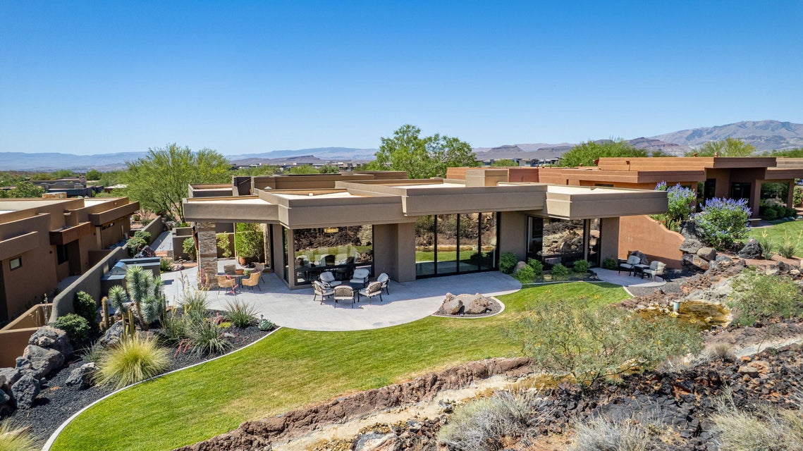 Contemporary desert architecture featuring expansive floor-to-ceiling windows, a spacious patio area, and a manicured lawn