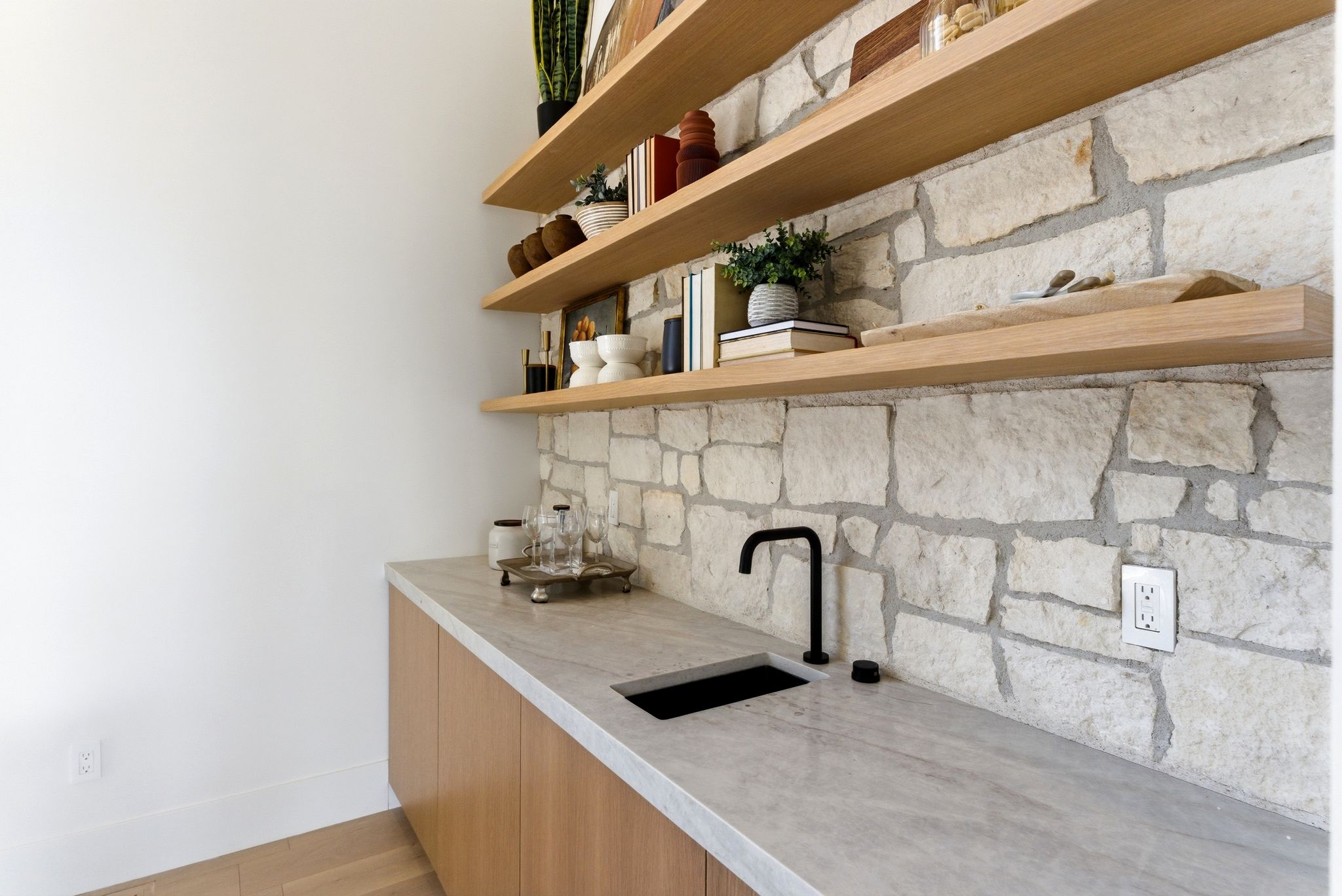 Built-in wet bar featuring a stone-clad backsplash, light wood-finish cabinetry, and a light-toned countertop