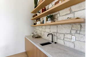 Built-in wet bar featuring a stone-clad backsplash, light wood-finish cabinetry, and a light-toned countertop