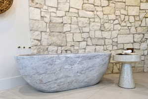 Freestanding stone bathtub with wall-mounted bronze fixtures