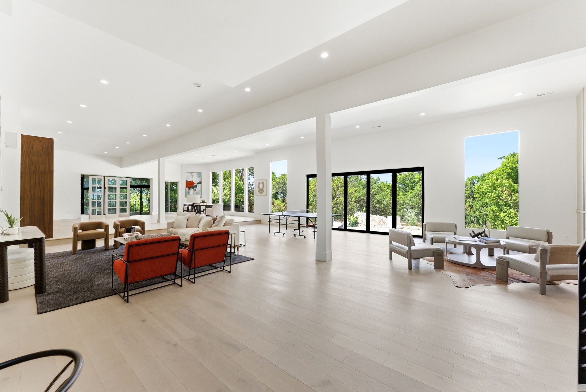 Expansive open-concept living space featuring high ceilings with recessed lighting, light wood-finish flooring, and multiple large windows and glass doors offering abundant natural light