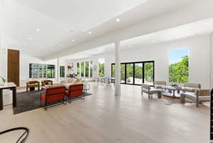 Expansive open-concept living space featuring high ceilings with recessed lighting, light wood-finish flooring, and multiple large windows and glass doors offering abundant natural light