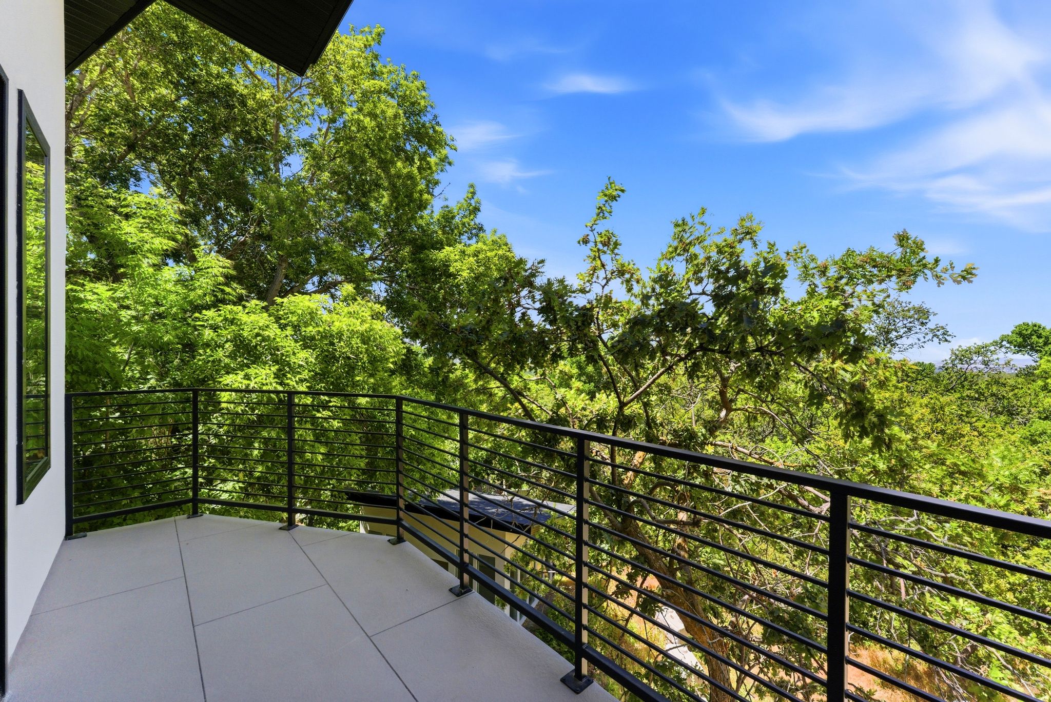 Exterior balcony featuring a concrete surface, black metal railing, and treetop surroundings