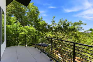 Exterior balcony featuring a concrete surface, black metal railing, and treetop surroundings