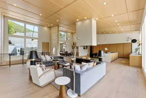 Spacious living area featuring light wood-finish flooring, a wood-paneled ceiling with recessed lighting, and expansive windows