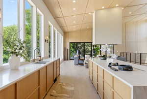 Modern kitchen featuring extensive natural wood-finish cabinetry, light-toned countertops, and a full wall of tall windows