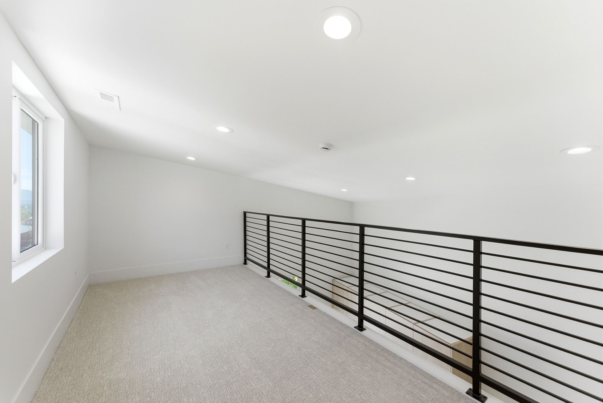 Upper level loft featuring a contemporary metal railing, recessed lighting, and a window providing natural light