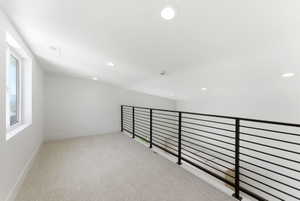 Upper level loft featuring a contemporary metal railing, recessed lighting, and a window providing natural light