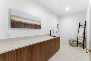Utility room featuring an elongated countertop with an integrated sink, wood-finish cabinetry, and light-toned tile flooring