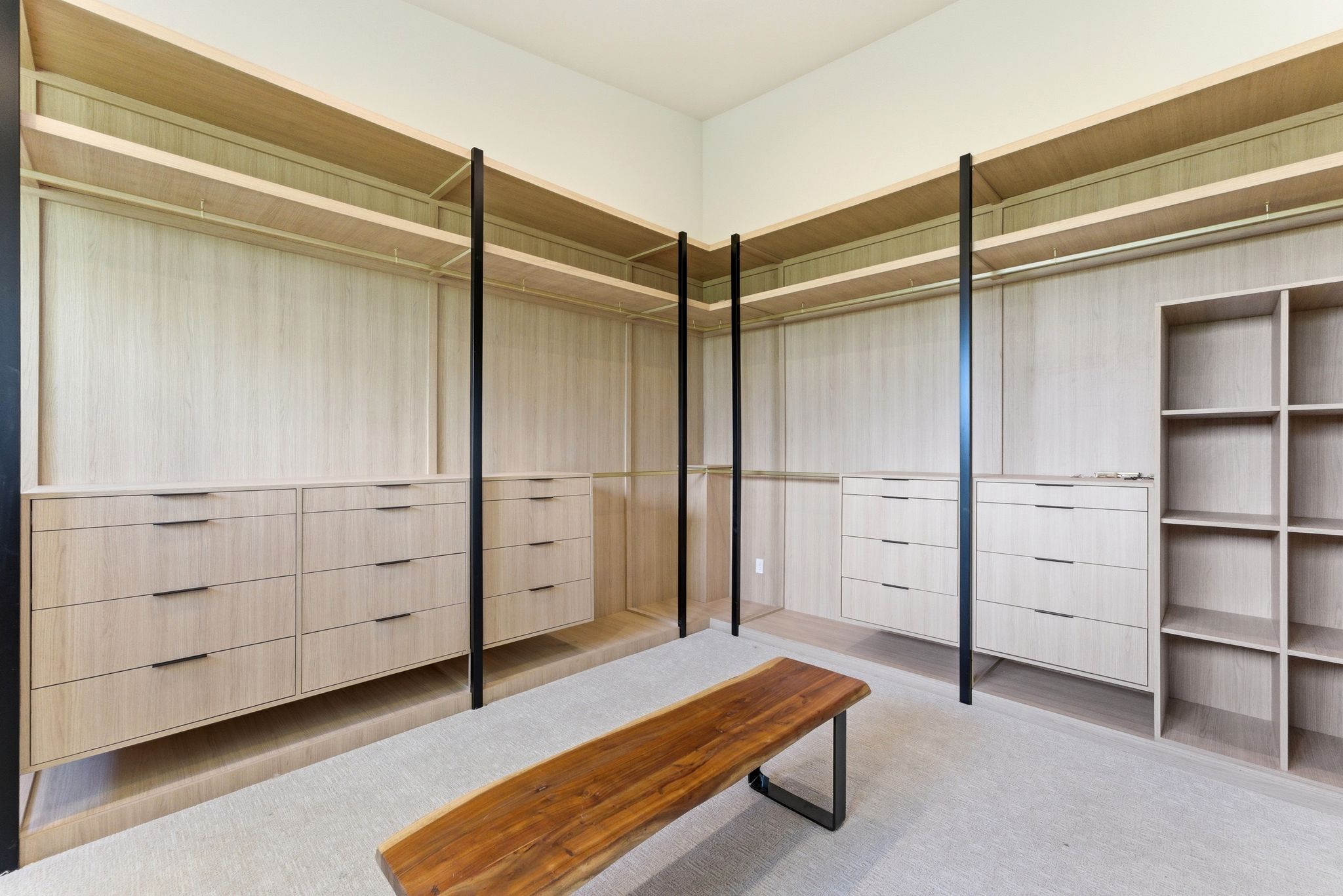 Custom closet system featuring light wood-finish cabinetry, integrated drawers with black hardware, open shelving, and full-height hanging rods
