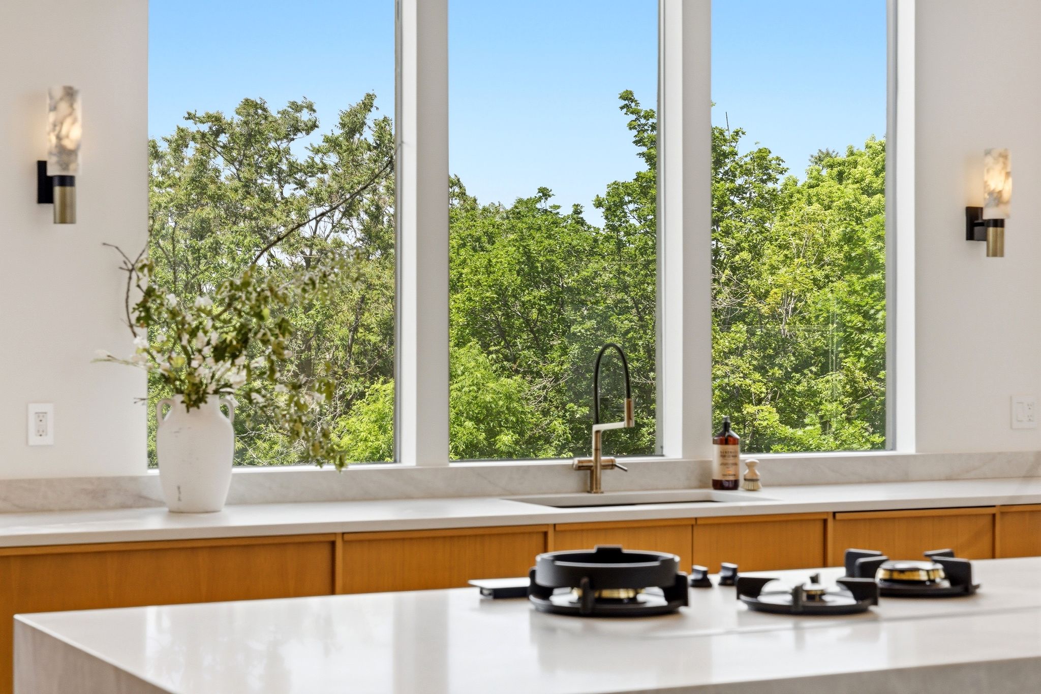 Kitchen featuring large pane windows, light wood-finish cabinetry, light-toned countertops, a built-in cooktop, and a wall-mounted faucet