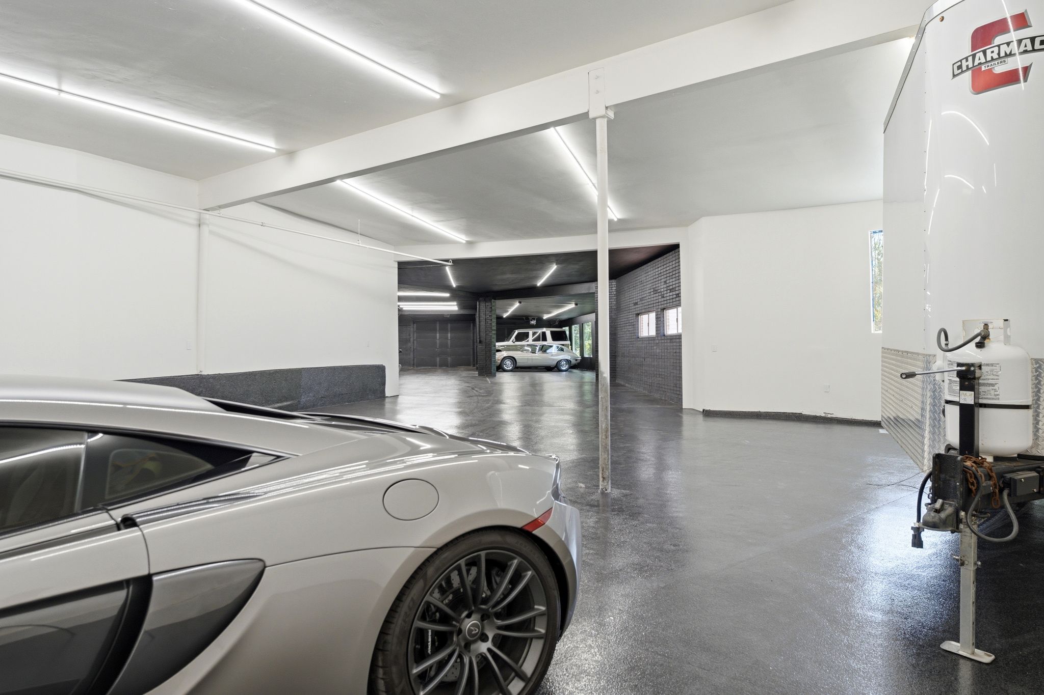 Spacious multi-vehicle garage with exposed structural beams, white painted walls, and overhead fluorescent lighting