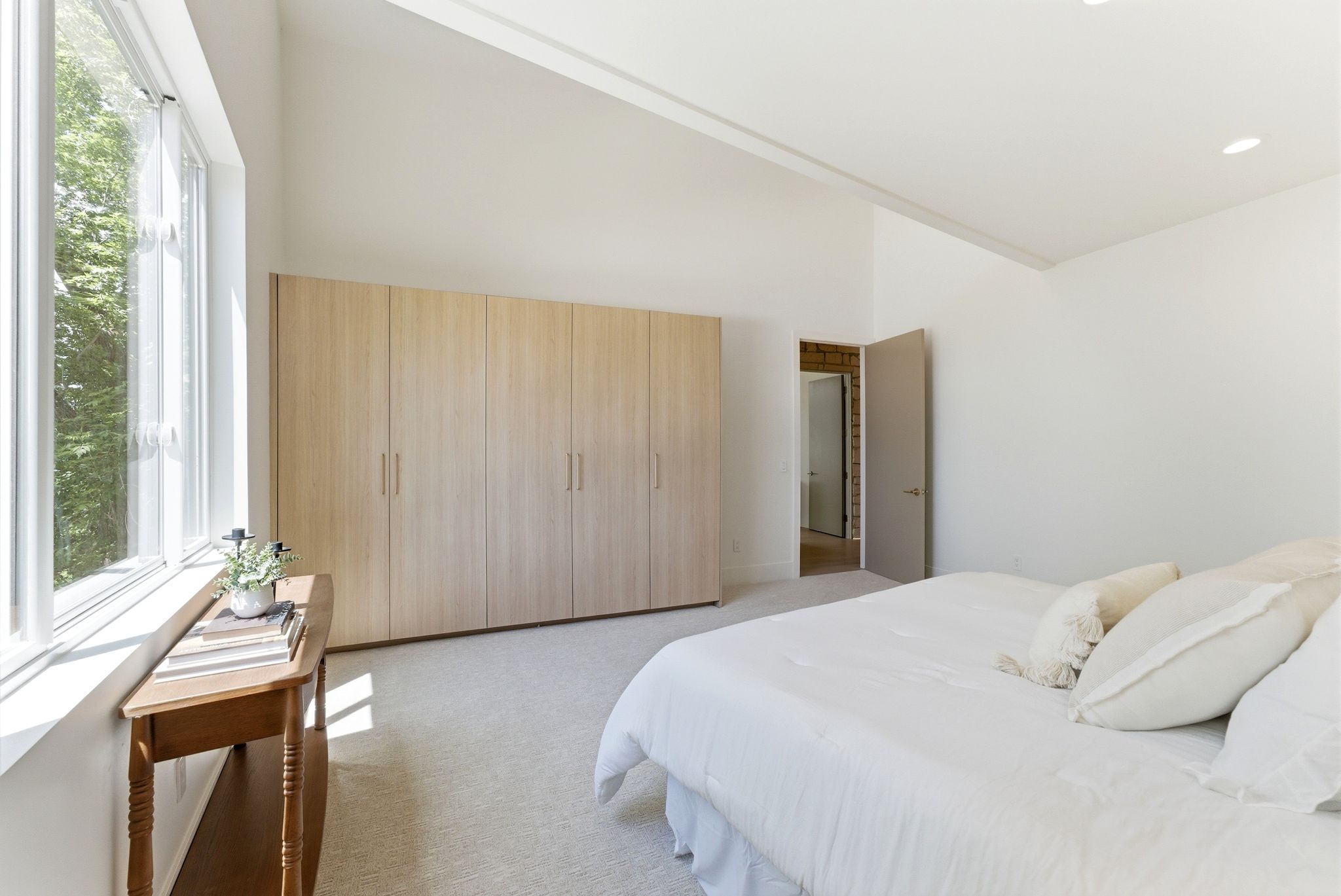 Spacious room featuring vaulted ceilings, recessed lighting, expansive windows, light wood-finish built-in wardrobe, and neutral carpeting
