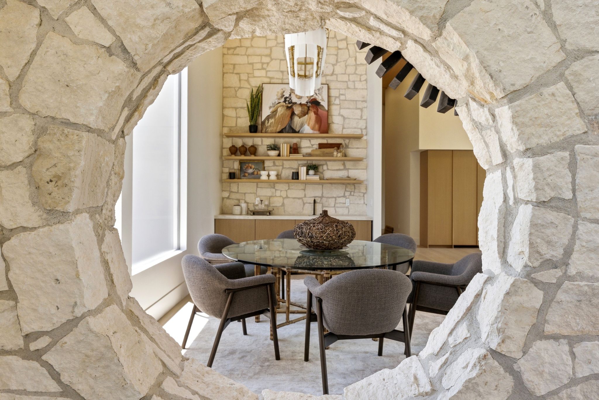Stone archway framing a dining area featuring a stone accent wall, built-in shelving, a glass-top table, and a contemporary light fixture