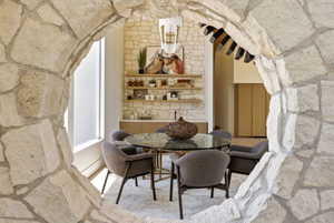 Stone archway framing a dining area featuring a stone accent wall, built-in shelving, a glass-top table, and a contemporary light fixture