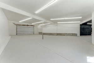 Spacious garage featuring a roll-up door, concrete flooring, ample overhead lighting, and white painted walls