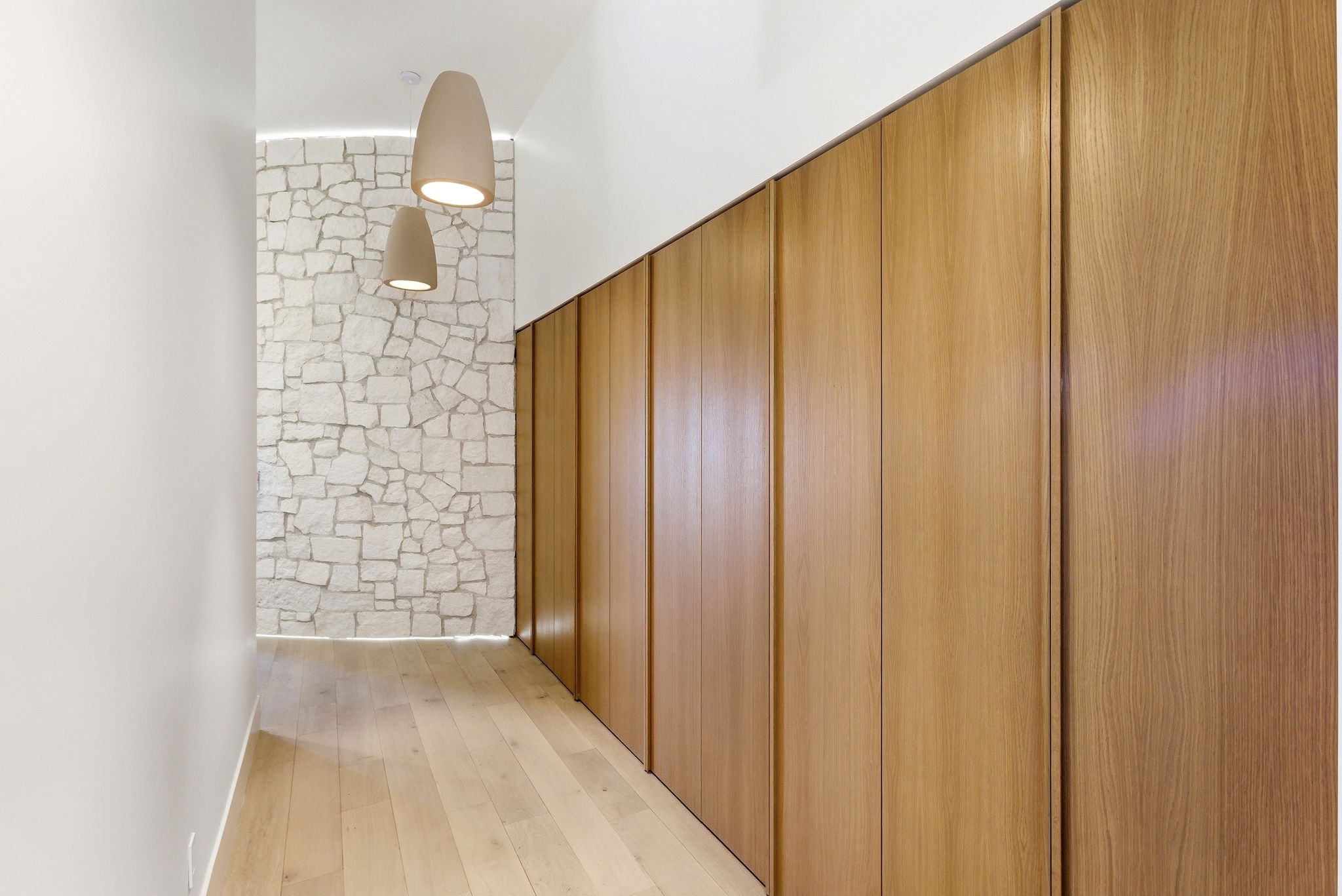 Hallway featuring warm wood-finish flooring, full-height wood-panel storage, and a stone accent wall