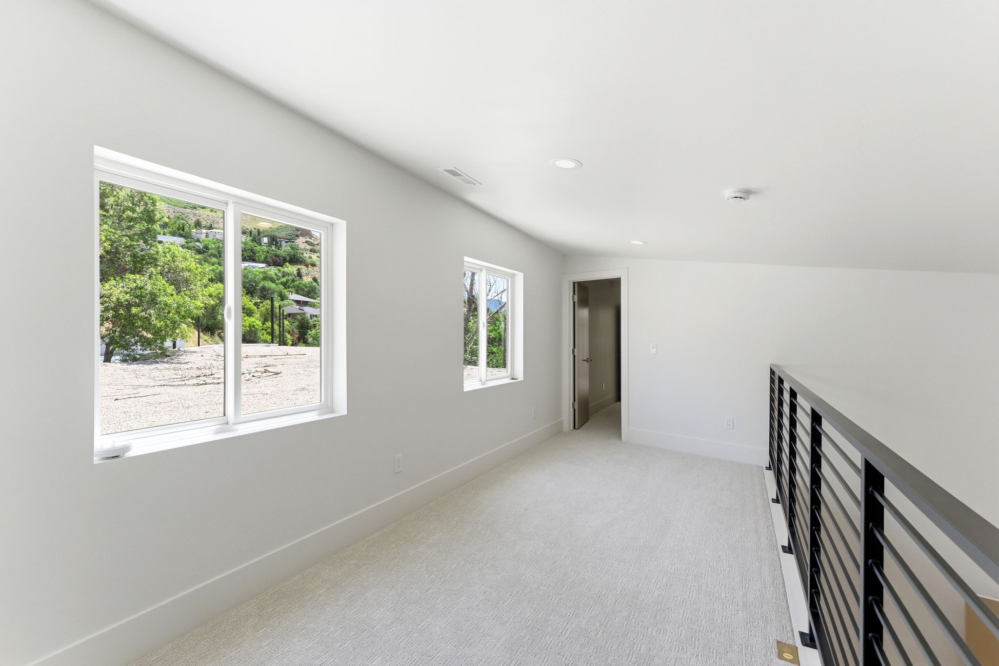 Loft area featuring light-toned carpet flooring, a modern black metal railing, and recessed ceiling lighting