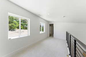 Loft area featuring light-toned carpet flooring, a modern black metal railing, and recessed ceiling lighting