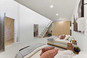 Open-concept room featuring a carpeted staircase with wood-finish risers, integrated wall lighting, built-in wooden cabinetry, and an exposed stone wall architectural feature