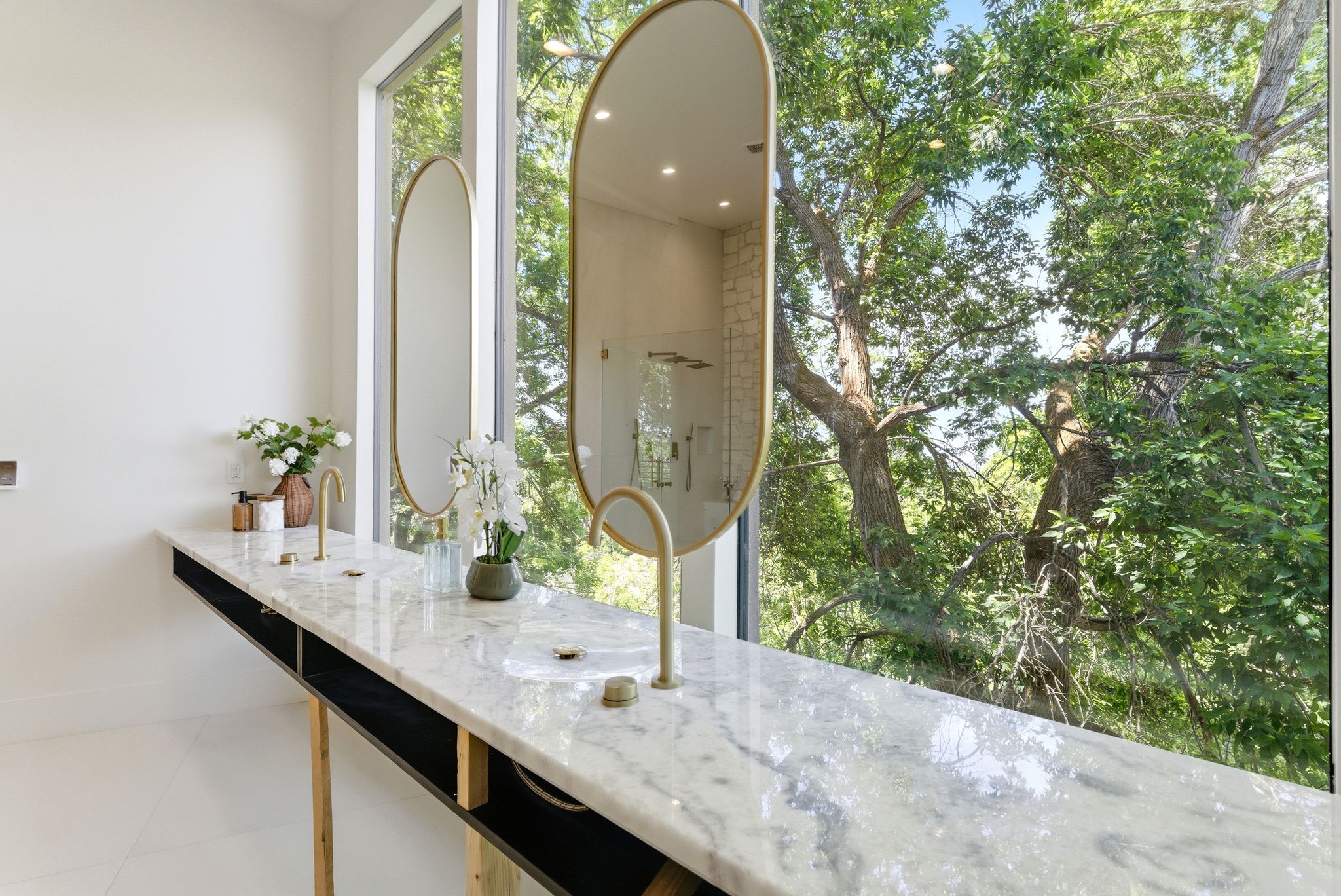Dual oval framed mirrors complement a floating vanity with a marble countertop