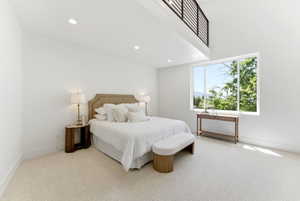 Bedroom featuring a large picture window, high ceilings, recessed lighting, neutral tone carpeting, and an overhead loft with a contemporary railing
