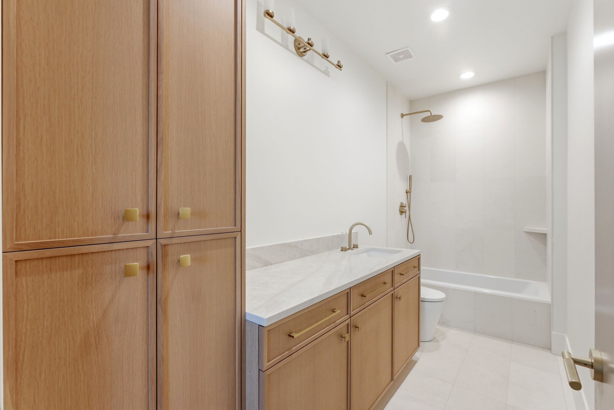 Bathroom featuring a wood-finish vanity with a light-toned countertop, a built-in tub with a shower system, recessed lighting, and integrated storage cabinetry