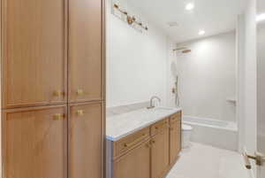 Bathroom featuring a wood-finish vanity with a light-toned countertop, a built-in tub with a shower system, recessed lighting, and integrated storage cabinetry