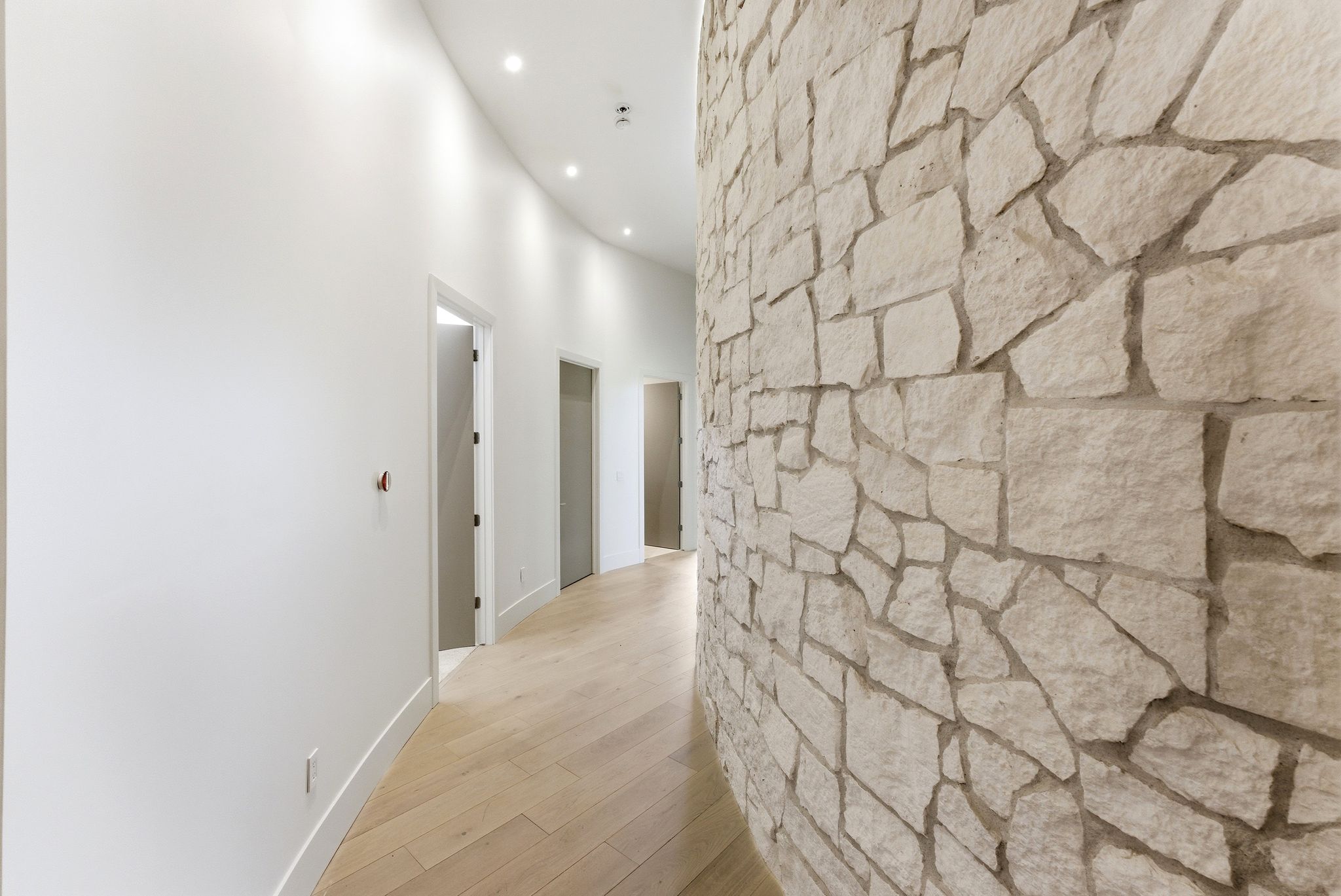 Curved hallway featuring a stone accent wall, recessed lighting, wood-finish flooring, and multiple doorways