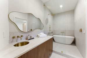 Contemporary bathroom with a freestanding tub, walk-in shower with glass enclosure, wood-finish vanity with an integrated basin, and gold-tone fixtures