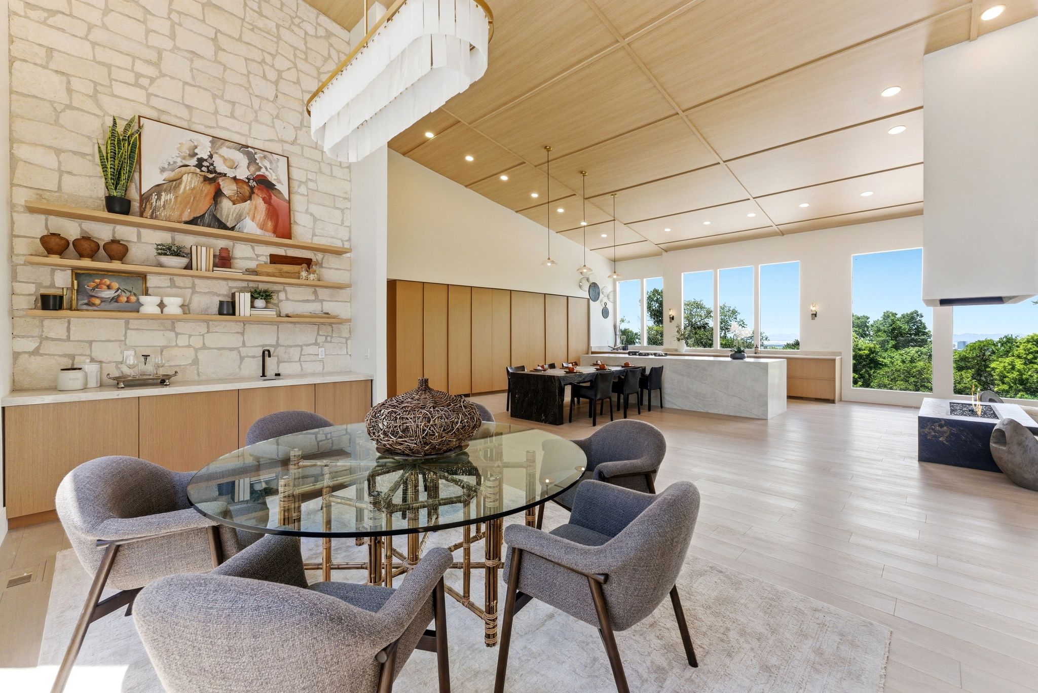 Spacious living area featuring light wood-finish flooring, a stone accent wall, a coffered ceiling, and large picture windows