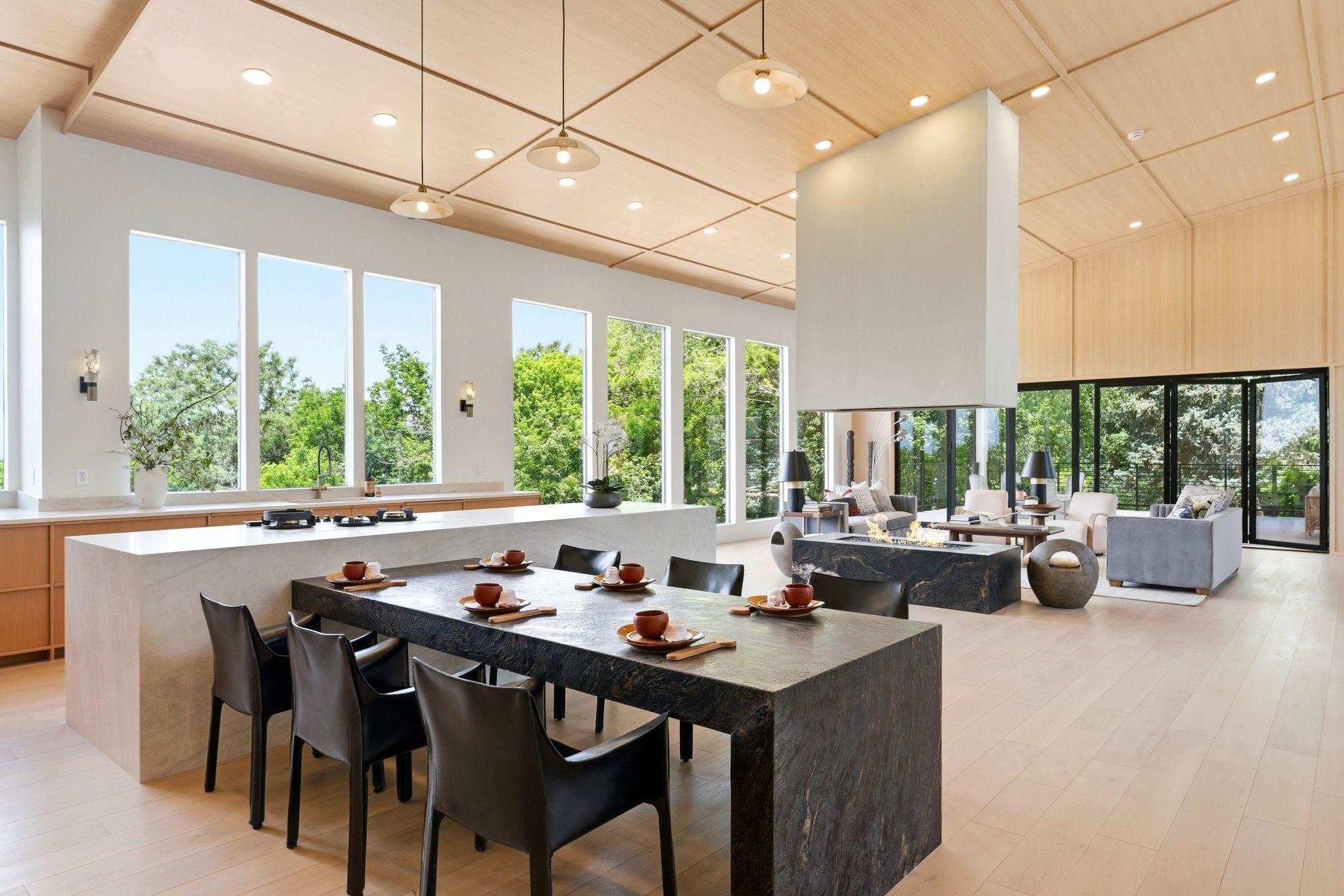 Open-concept living space featuring light wood-finish flooring, a wood-paneled vaulted ceiling, and a large central fireplace