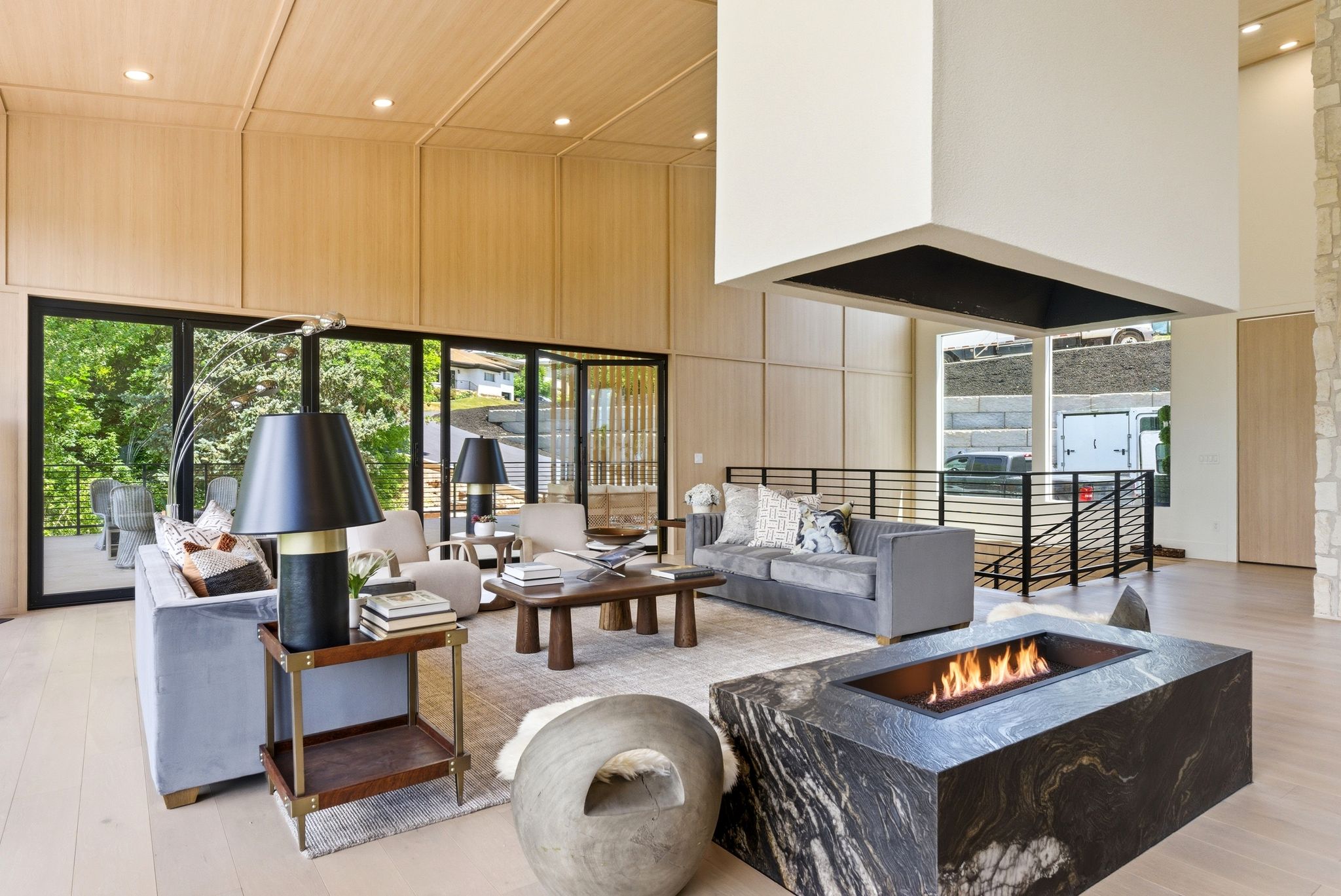 Spacious living area featuring a black marble-style fireplace, light wood-finish flooring, and expansive glass doors