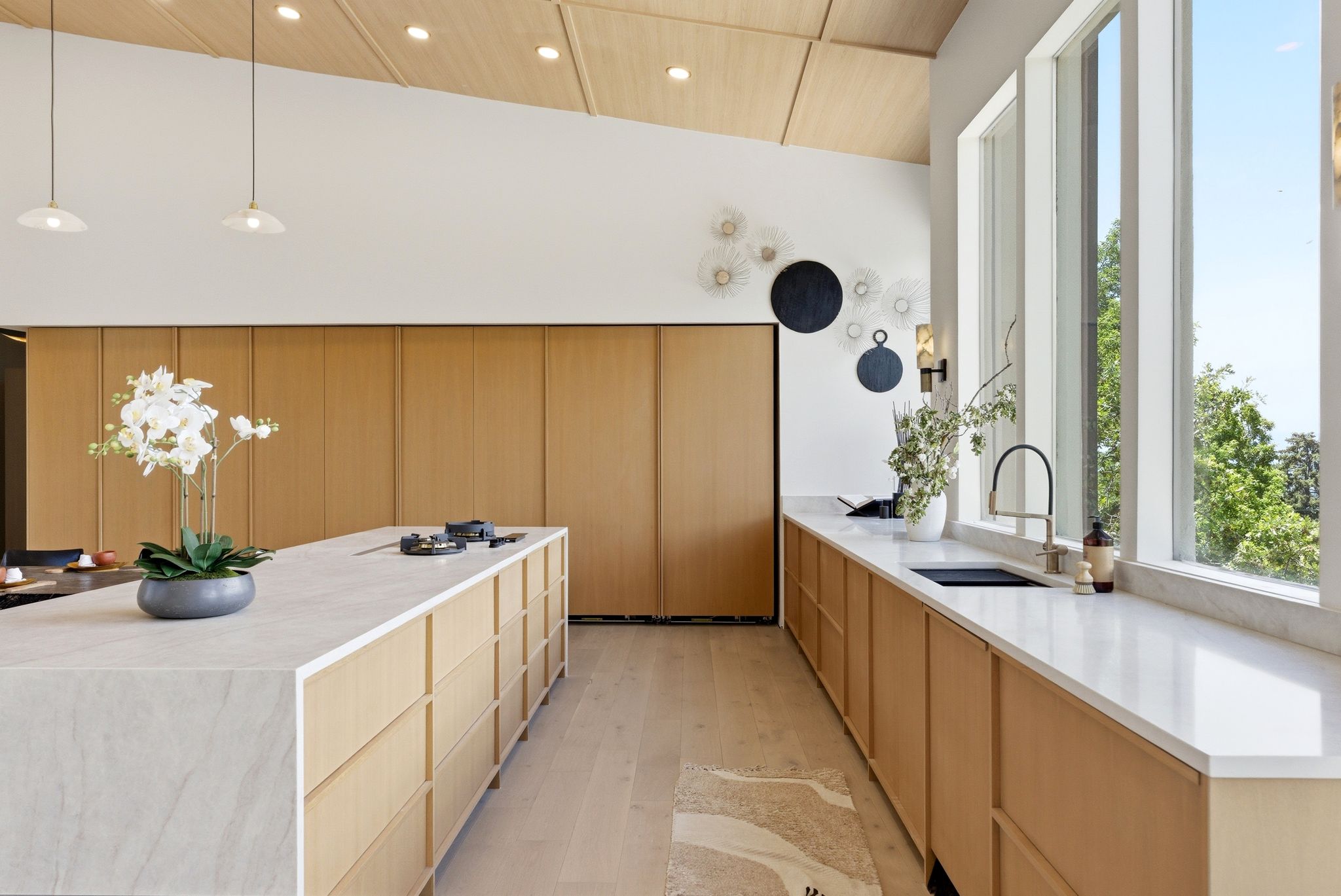Contemporary kitchen featuring an expansive center island with integrated cooktop, extensive countertop space with an undermount sink, and full-height wood-panel cabinetry