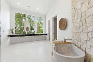Spacious bathroom featuring a freestanding stone soaking tub, a full-height stone accent wall, and expansive windows